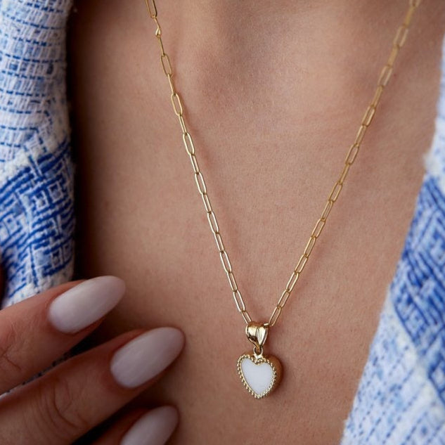 A close-up image of a 14k gold heart necklace with a paperclip chain, worn around a person's neck.